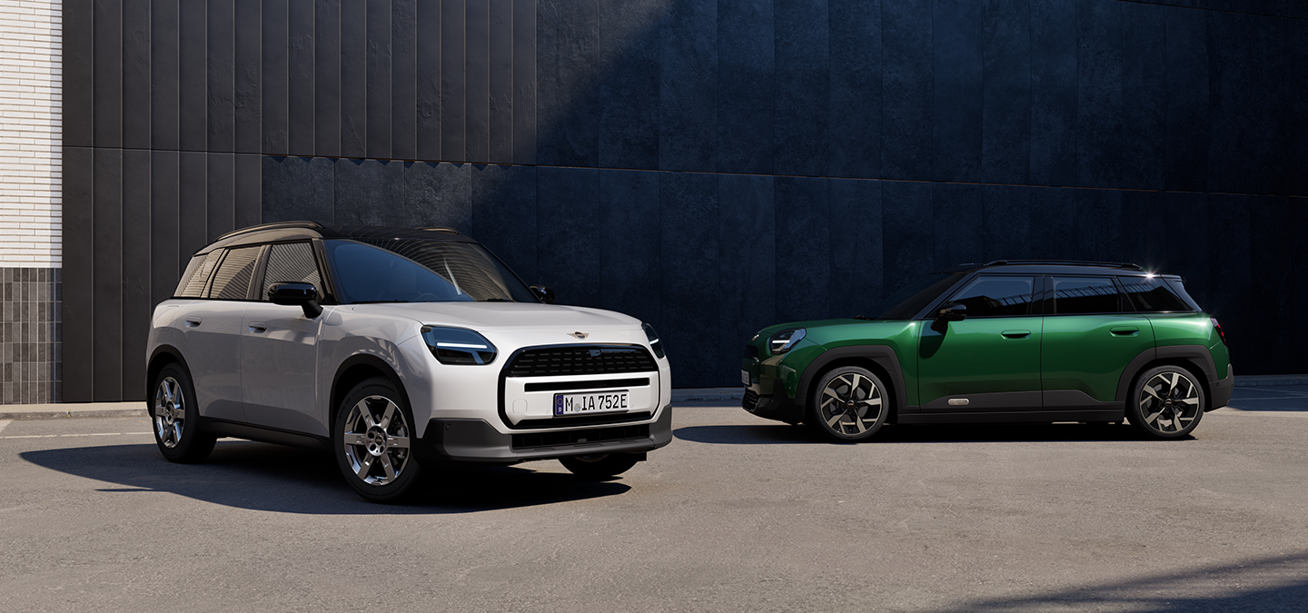 Voor- en zijaanzicht van de MINI Aceman Electric in Nanuq White en British Racing Green met dak in Black, in een straat.