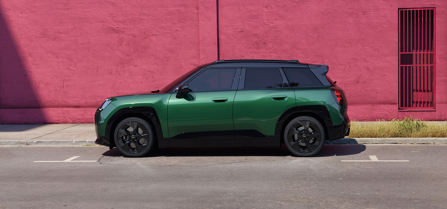 Zijaanzicht van de MINI Aceman Electric in British Racing Green met dak in Black, in een straat.