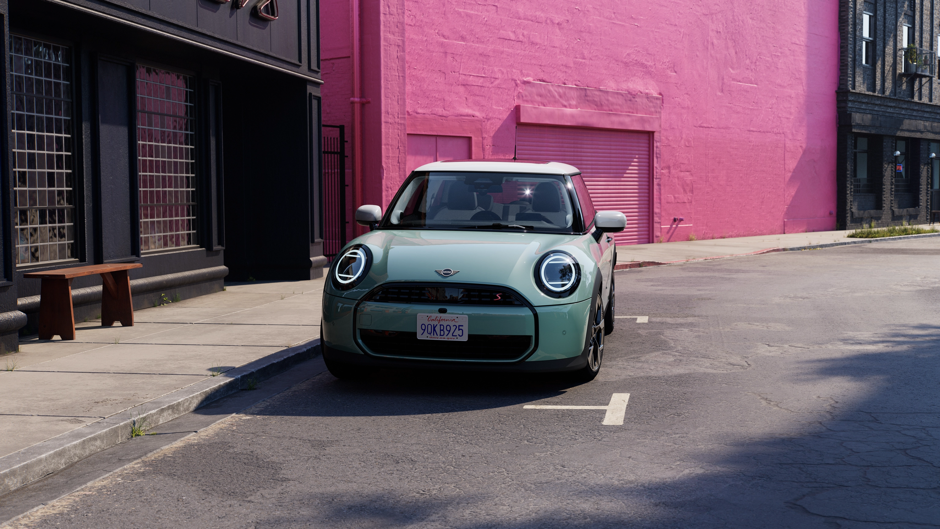 Vooraanzicht van een parkerende MINI Cooper in Ocean Wave Green en een dak in het White op straat met een roze muur op de achtergrond