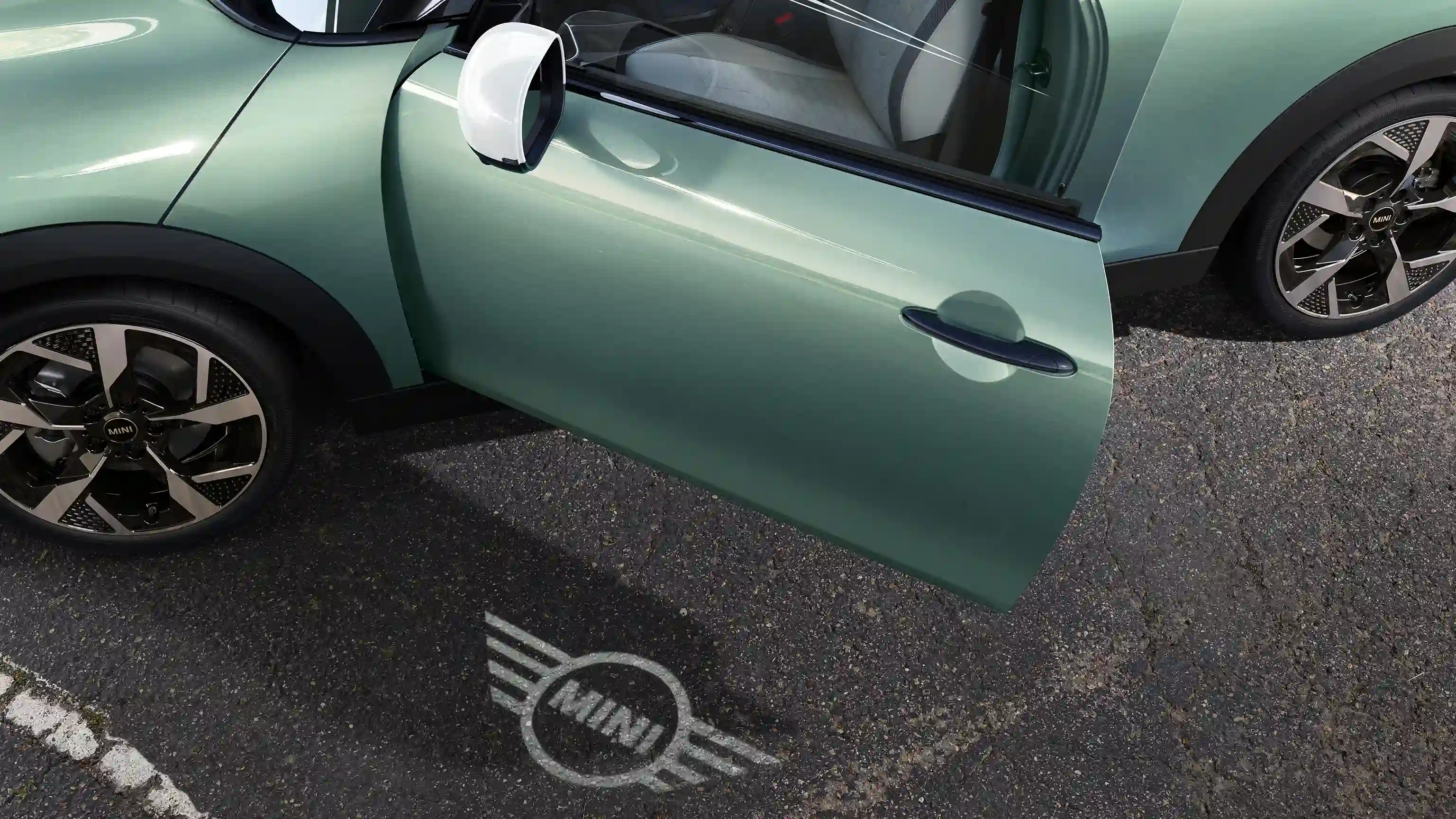 Buitenaanzicht van de MINI Cooper met een geopende deur en verlicht MINI logo op de grond 