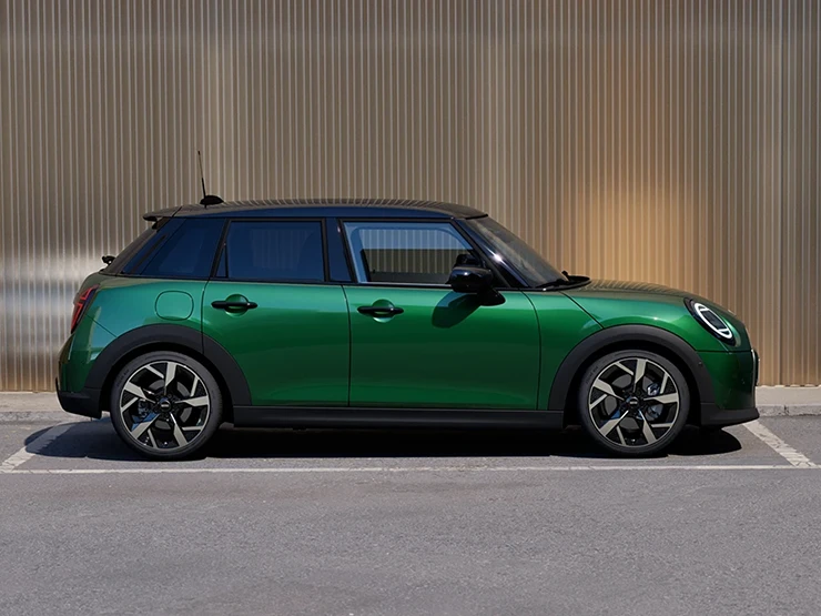 Zijaanzicht van een parkerende MINI Cooper 5-deurs in British Racing Green met dak in Black.