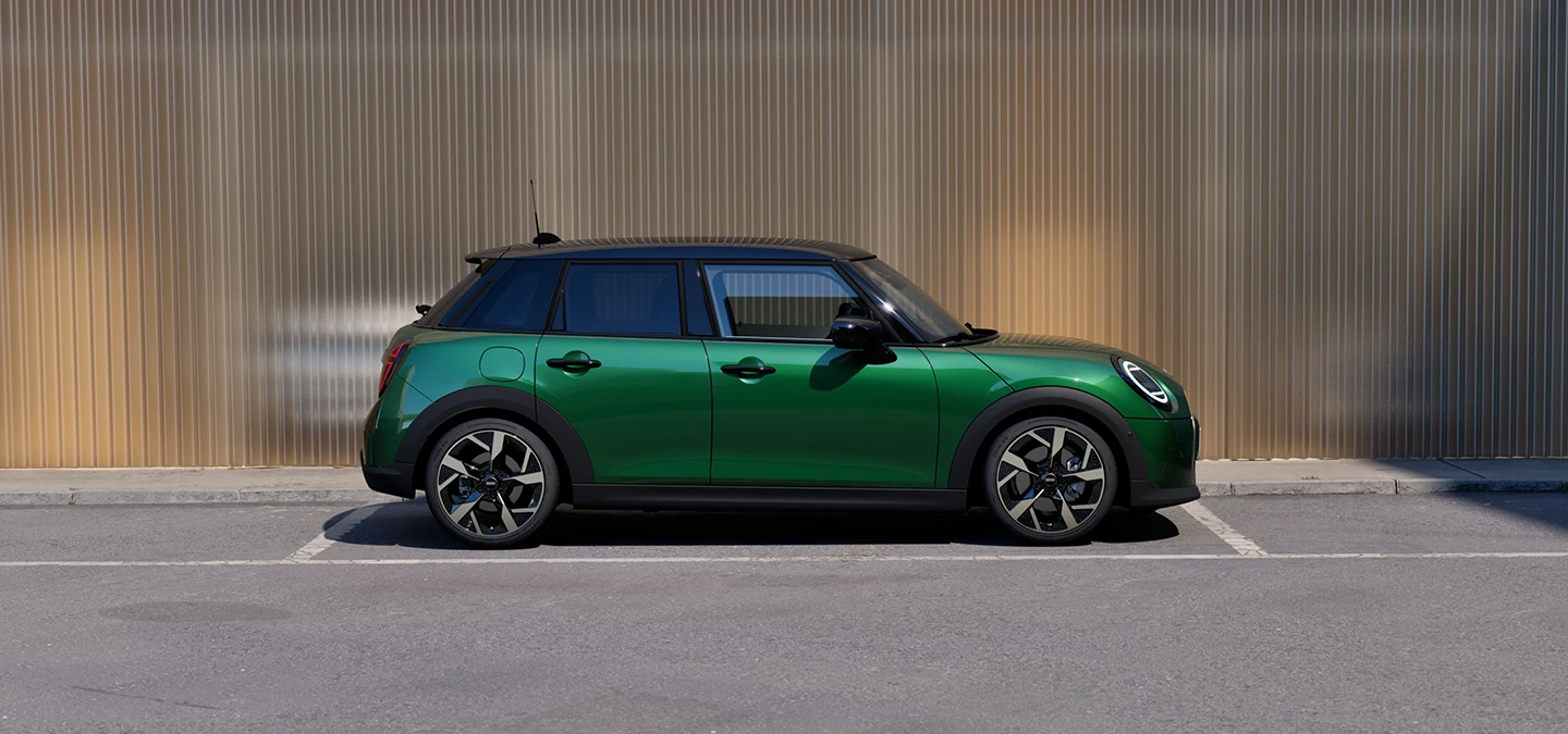 Zijaanzicht van een parkerende MINI Cooper 5-deurs in British Racing Green met dak in Black.