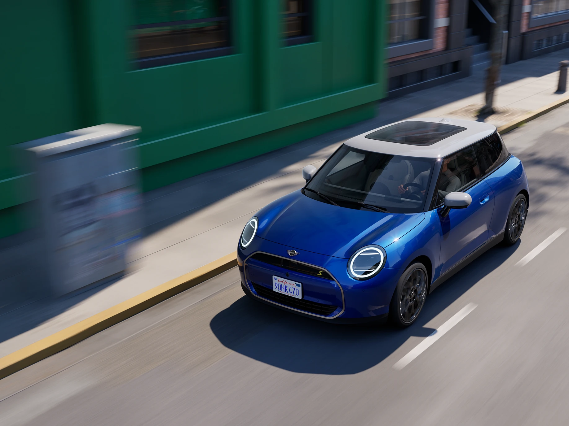 Bovenaanzicht van een in een straat rijdende MINI Cooper Electric in Blazing Blue met dak in White. 