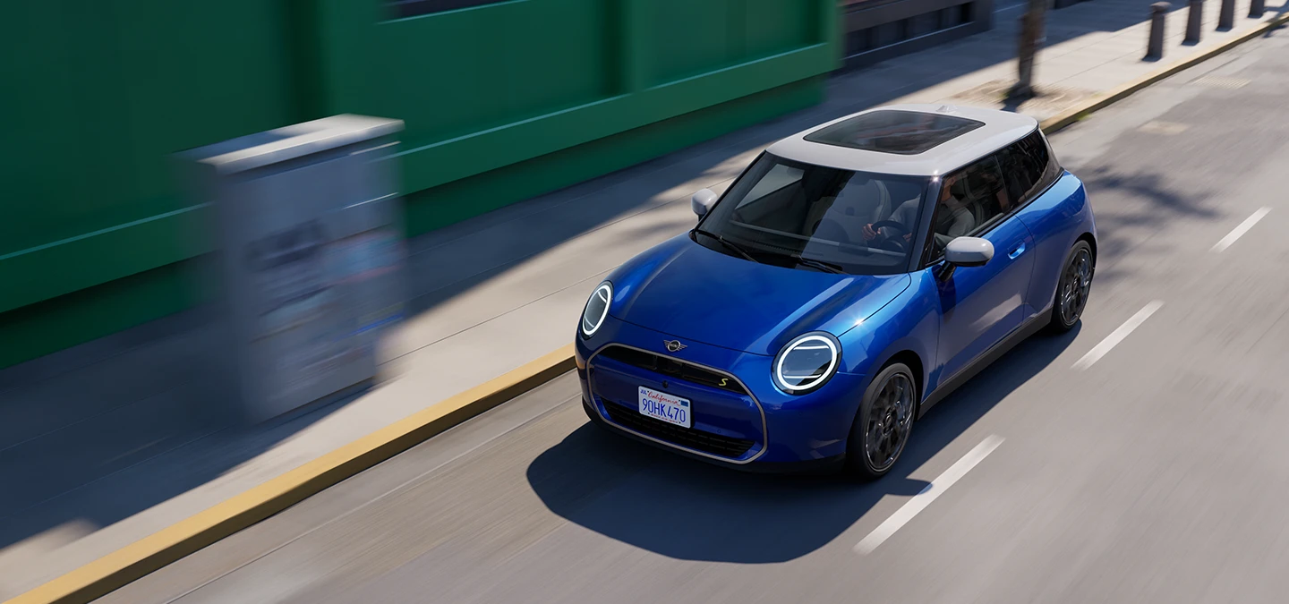 Bovenaanzicht van een in een straat rijdende MINI Cooper Electric in Blazing Blue met dak in White. 