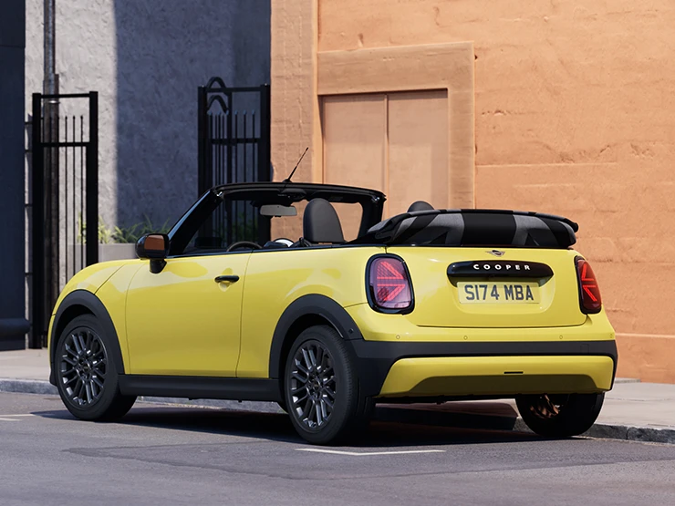 Aanzicht links van achteren op een geparkeerde MINI Cooper Cabrio in Sunnyside Yellow.