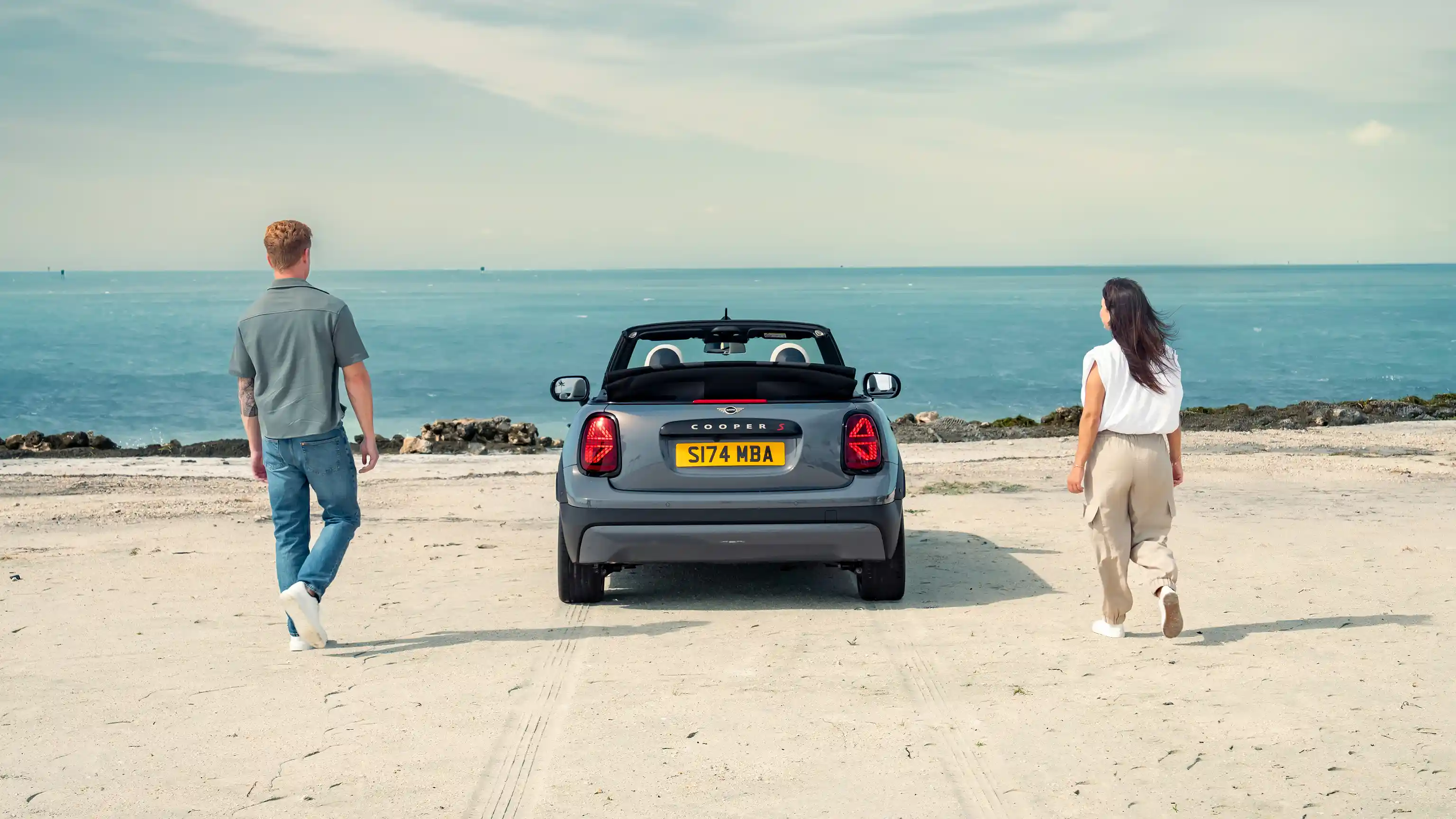 Achteraanzicht van een parkerende MINI Cooper Cabrio op een strand met twee mensen