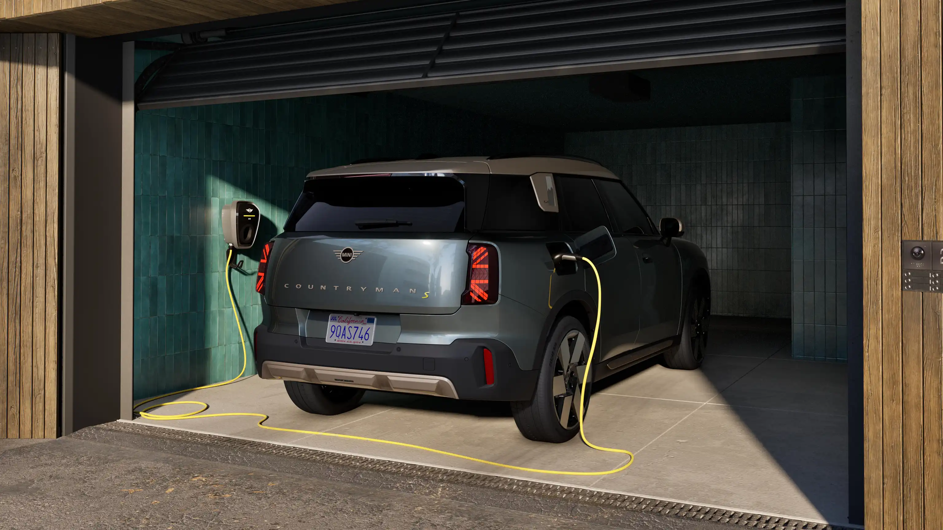 Achteraanzicht van een opladende volledig elektrische MINI Countryman in Smokey Green, in een geopende garage met een aangesloten laadkabel.
