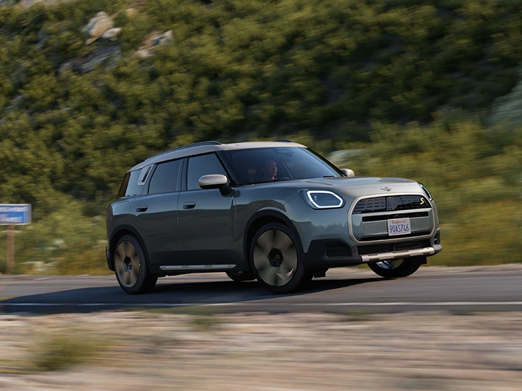 Zijaanzicht van een off-road rijdende MINI Countryman Electric in Smokey Green met dak in Vibrant Silver.