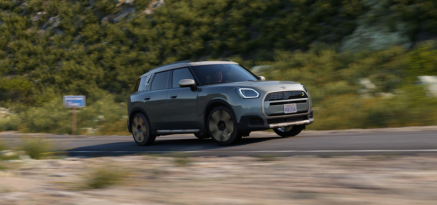 Zijaanzicht van een off-road rijdende MINI Countryman Electric in Smokey Green met dak in Vibrant Silver.