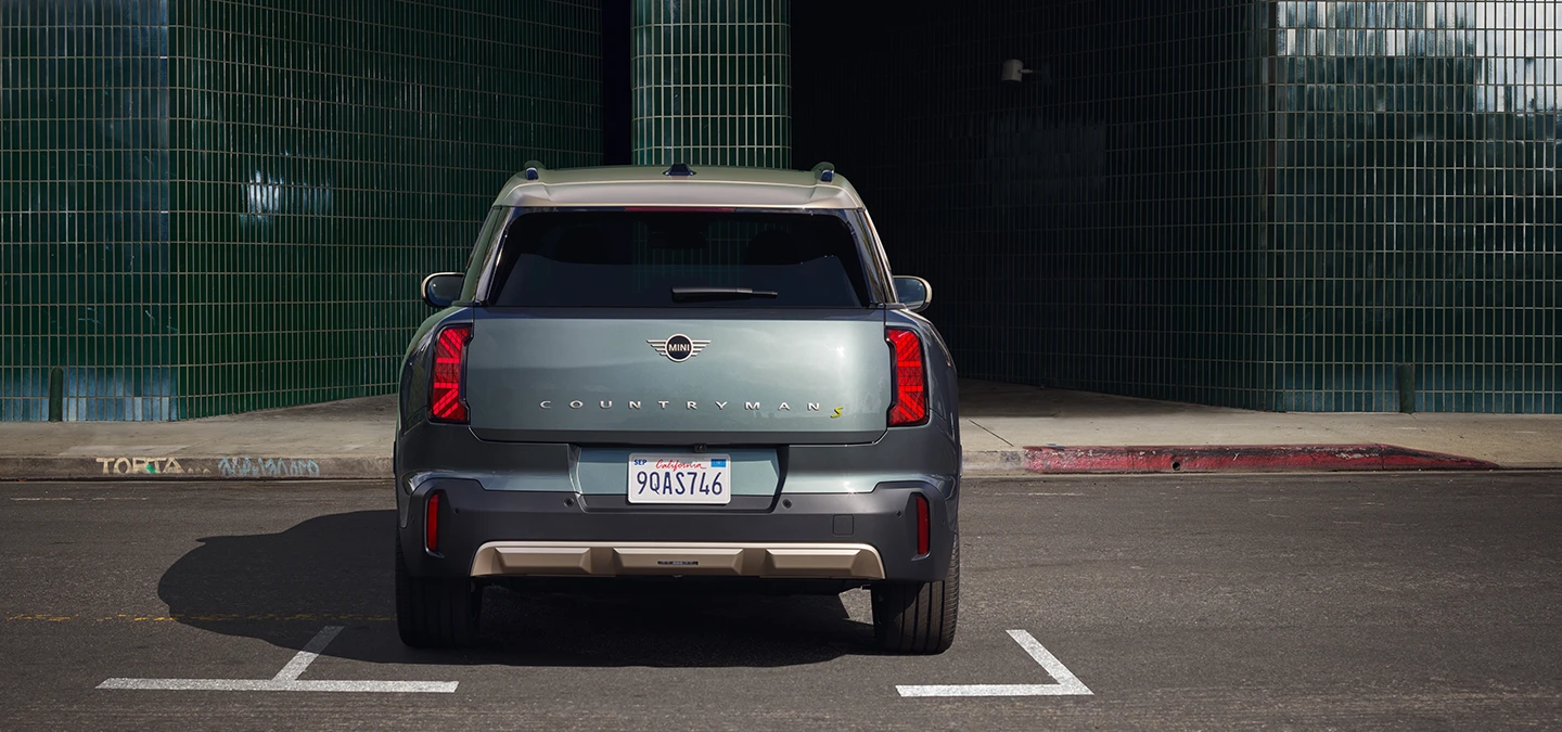Achteraanzicht van een parkerende MINI Countryman Electric in Smokey Green met dak in Vibrant Silver. 