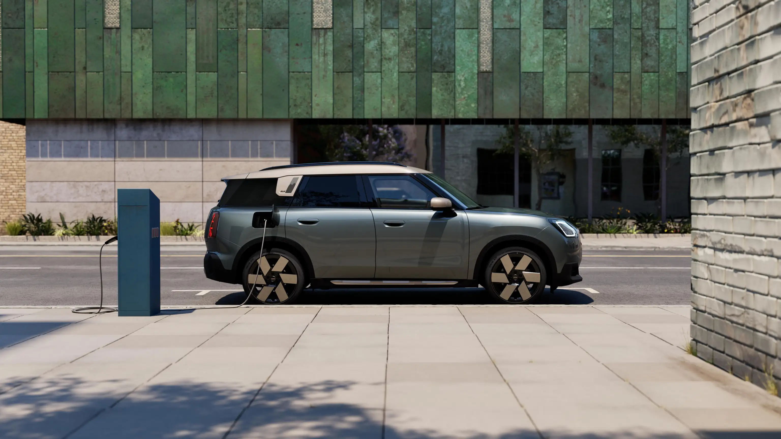 Zijaanzicht van een opladende volledig elektrische MINI Countryman in Smokey Green met een dak in Vibrant Silver