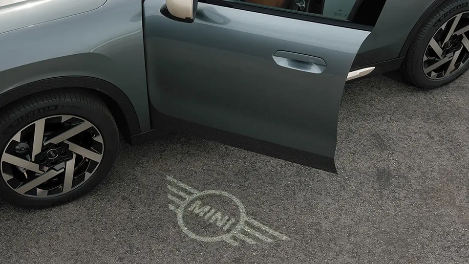 Buitenaanzicht van MINI Countryman met geopende deur en verlicht MINI logo op de grond