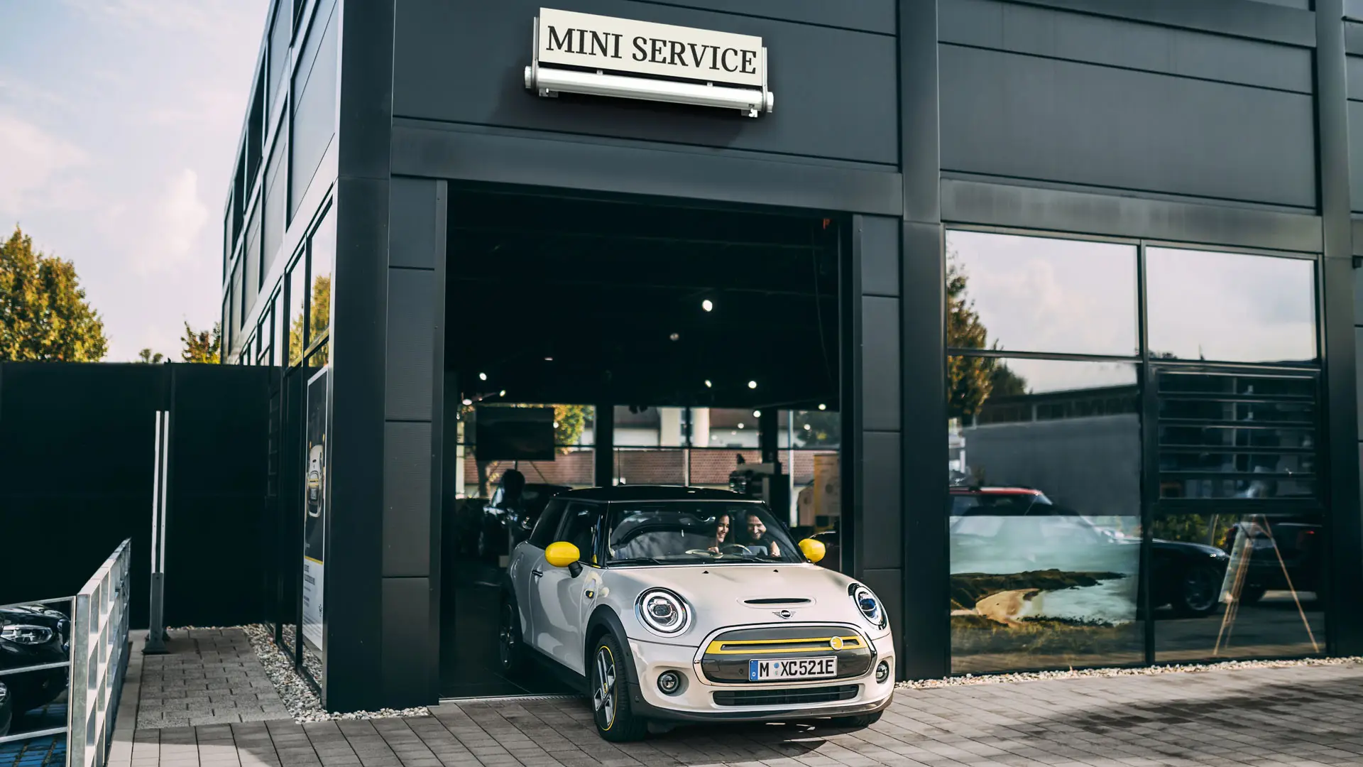 Terrein van MINI servicepartner met een klant die haar nieuwe MINI Electric naar het voorplein rijdt
