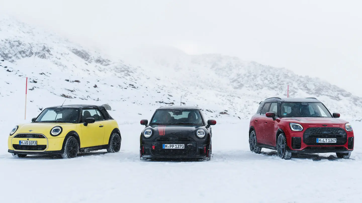 MINI Cooper Cabrio in Sunny Side Yellow, MINI John Cooper Works in Midnight Black II en MINI Countryman Cooper in Chili Red — stilstaand op een besneeuwde bergweg, vooraanzicht.
