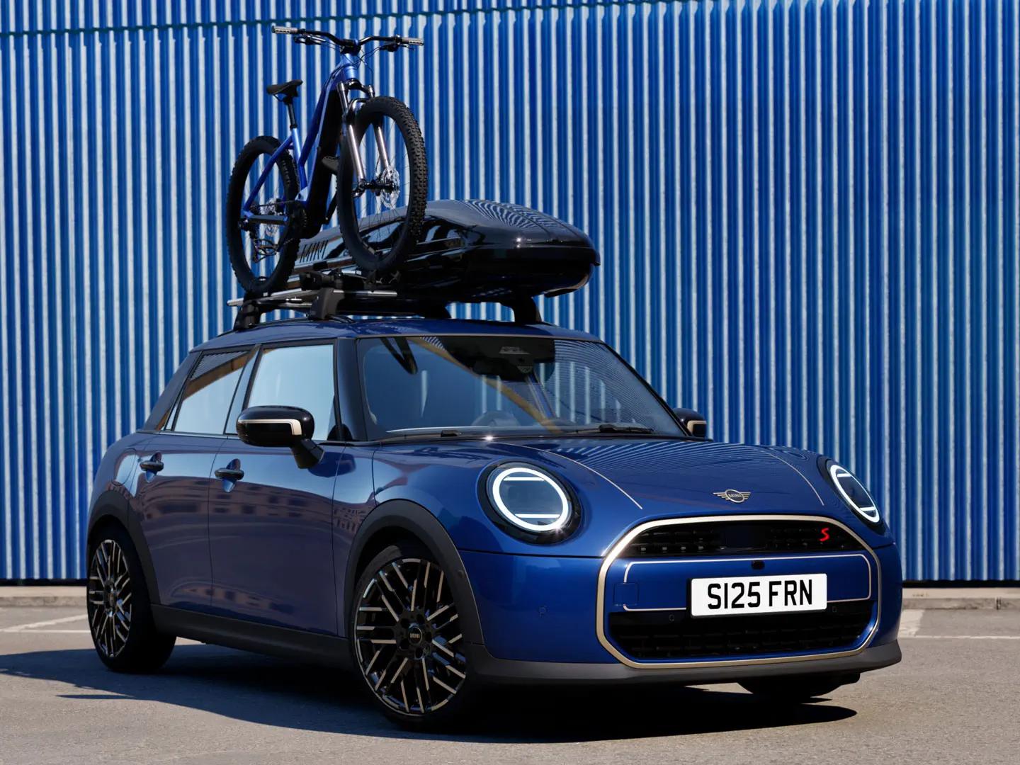 Vooraanzicht van MINI Aceman in Indigo Sunset Blue met MINI dakfietsendrager met mountainbike en MINI dakkoffer 320.