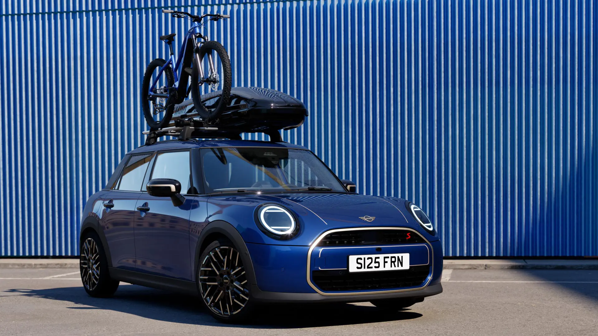 Vooraanzicht van MINI Aceman in Indigo Sunset Blue met MINI dakfietsendrager met mountainbike en MINI dakkoffer 320.