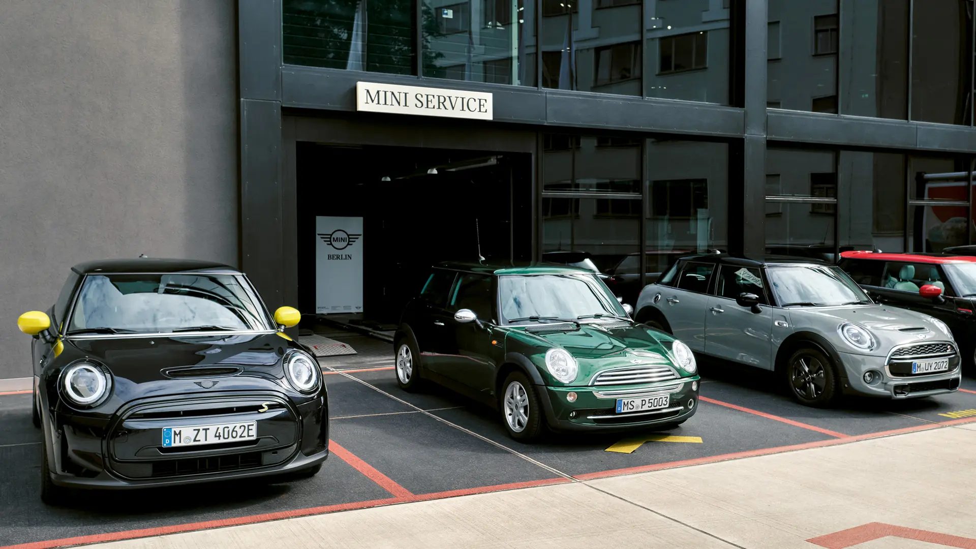 MINI Cooper Electric S in het zwart voor een MINI dealer naast een MINI Cooper 3-deurs in het groen, de MINI 5-deurs in het zilver, de MINI JCW zwart, vooraanzicht. 