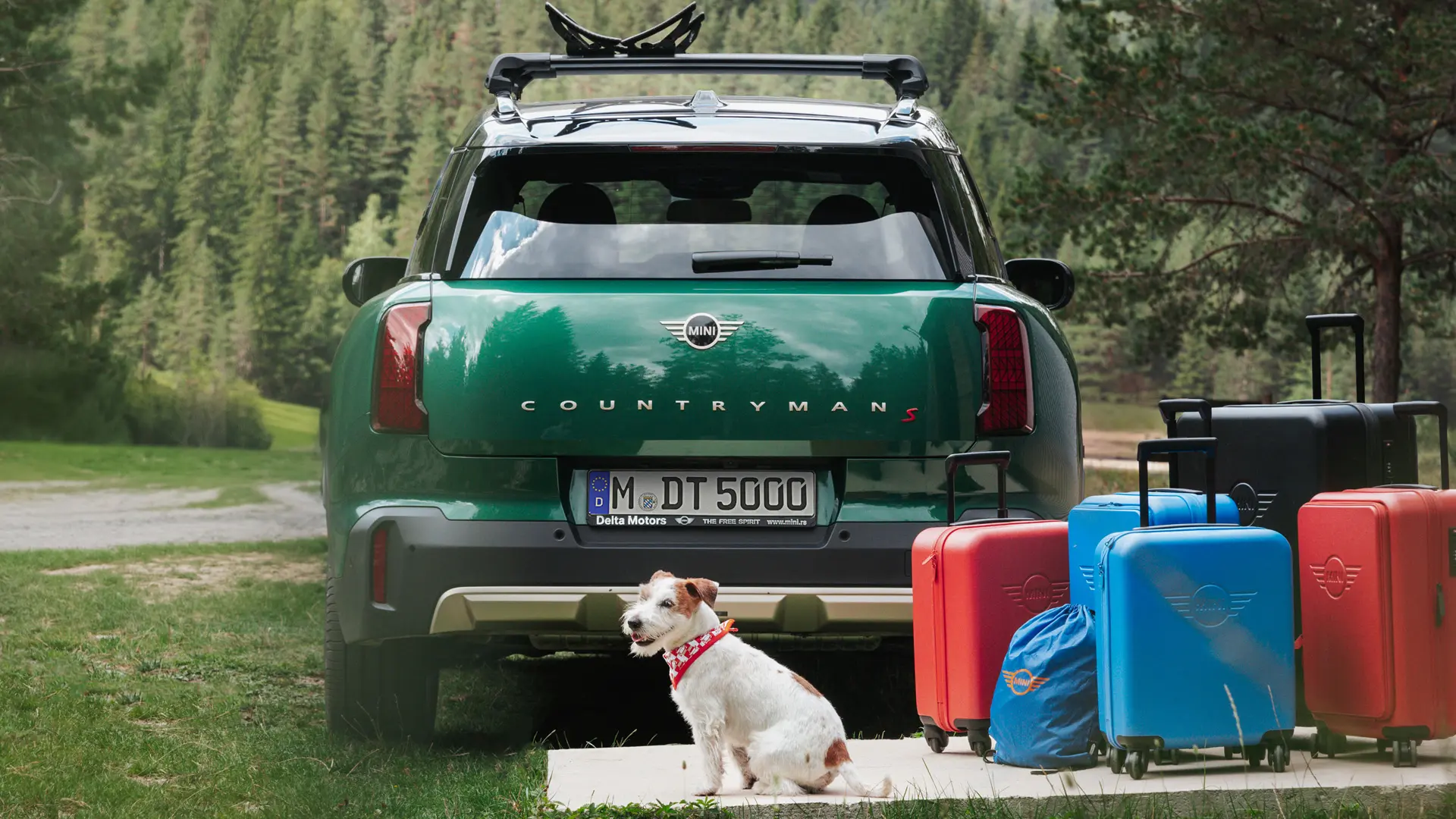 MINI Countryman in het groen met daarachter verschillende soorten bagage, die gekocht kunnen worden in de MINI Lifestyle store, en een jack russell. 