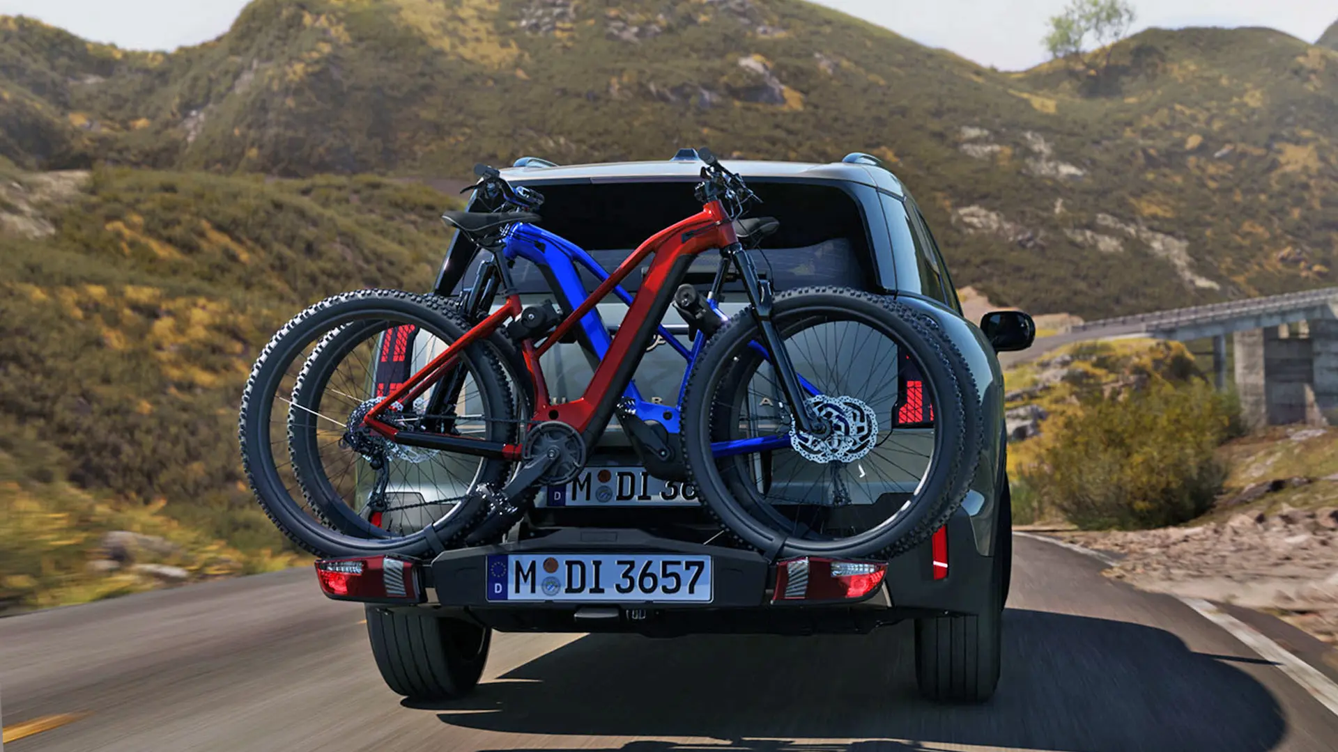 MINI Countryman in Smokey Green uitgerust met de fietsendrager voor achterop met twee mountainbikes, achteraanzicht, rijdend over een bergweg.