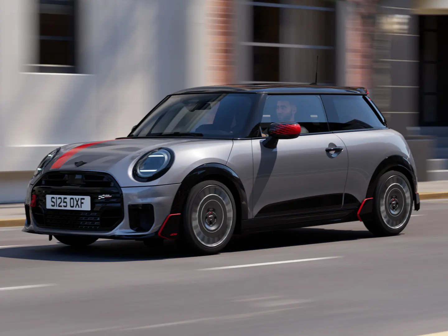 MINI Cooper 3-deurs in Melting Silver met John Cooper Works- buitenspiegelkap en motorkapsticker in Chili Red, dakspoiler en winglet in zwart, rijdt in de stad — zijaanzicht van voor.
