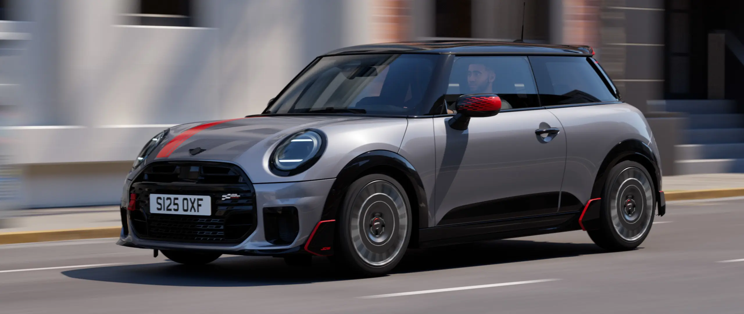 MINI Cooper 3-deurs in Melting Silver met John Cooper Works- buitenspiegelkap en motorkapsticker in Chili Red, dakspoiler en winglet in zwart, rijdt in de stad — zijaanzicht van voor.