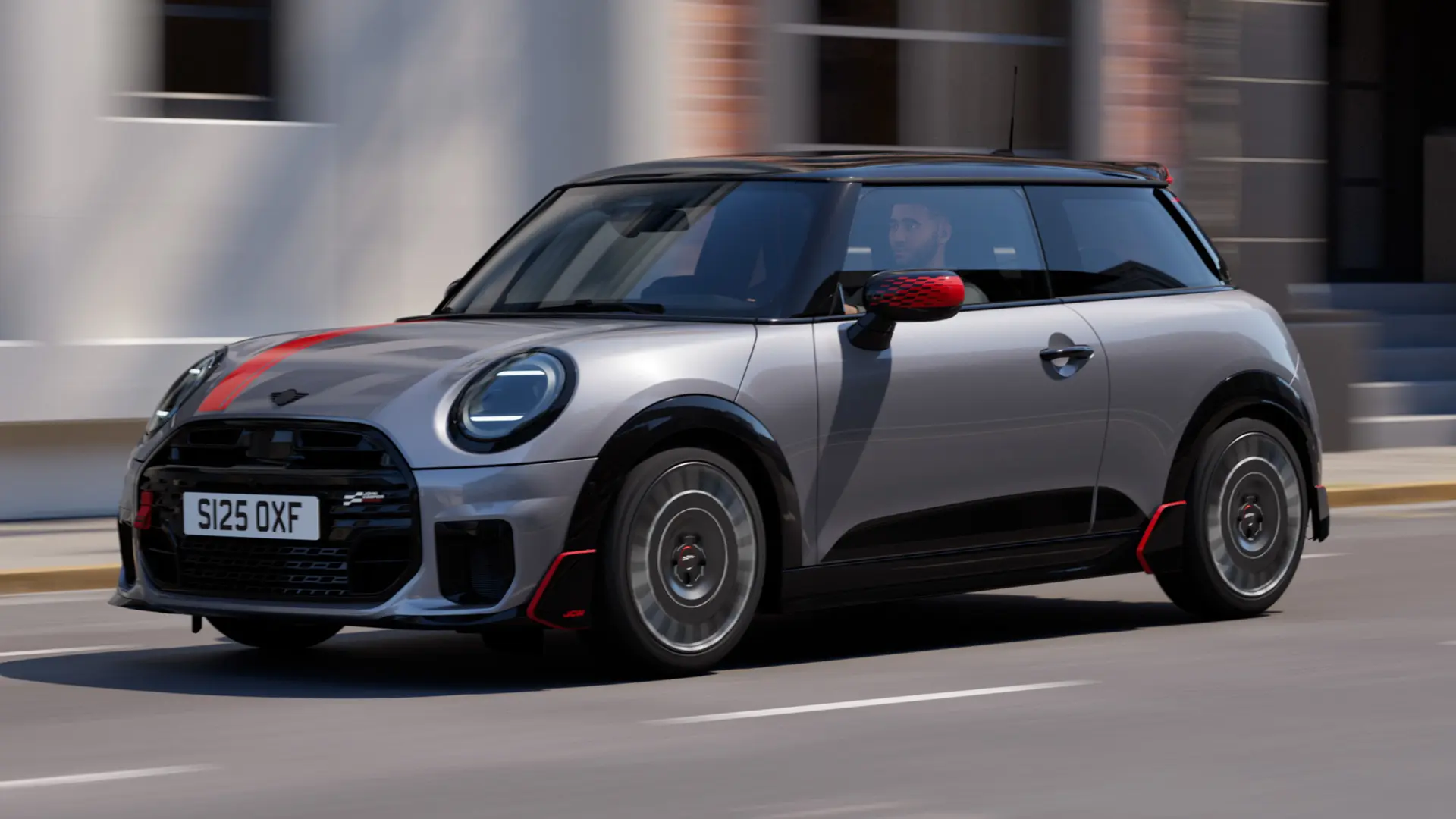 MINI Cooper 3-deurs in Melting Silver met John Cooper Works- buitenspiegelkap en motorkapsticker in Chili Red, dakspoiler en winglet in zwart, rijdt in de stad — zijaanzicht van voor.