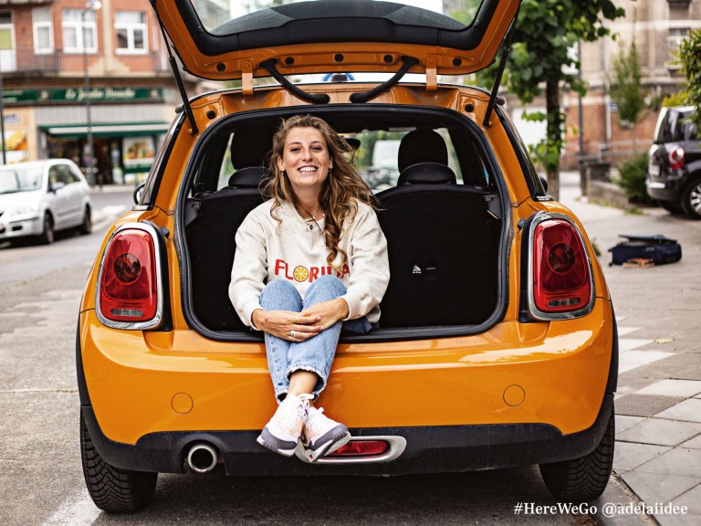 MINI 3-deurs hatchback in volcanic orange met blije dame in de kofferbak.